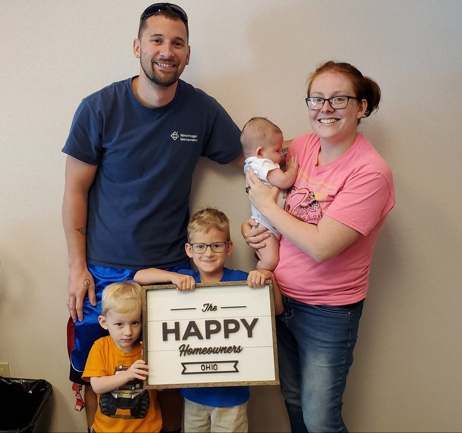 A family of five with a new-home sign on closing day