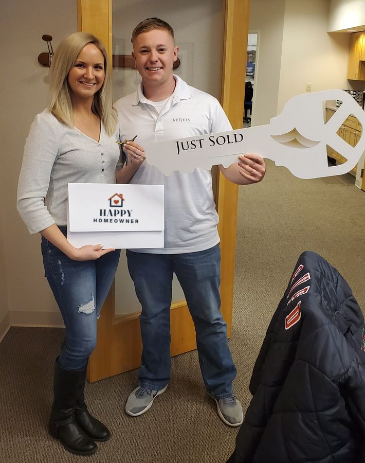 A young couple holding a Just Sold key and their closing folder