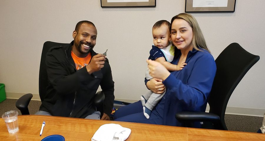 A new homeowner holding up keys next to his partner and baby