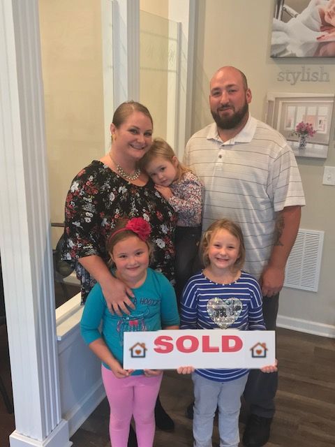 A family of five with their girls holding a Sold sign